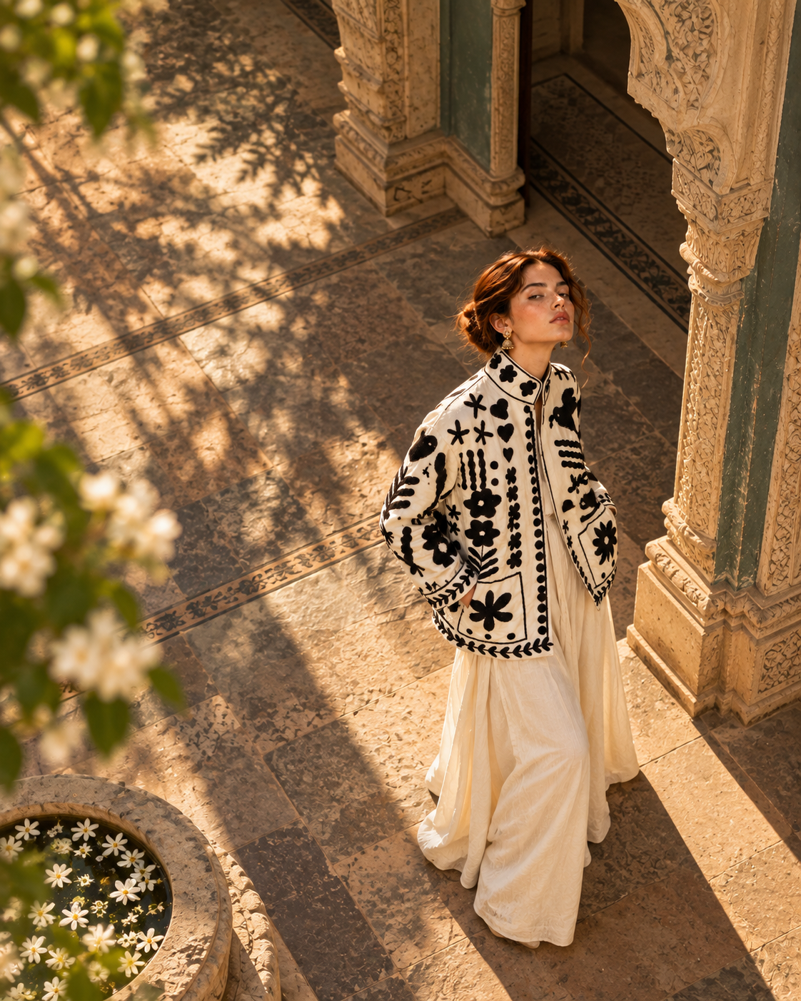 Seen from above, a model in the Siyah Phool jacket standing in a sunlit courtyard beside a carved column